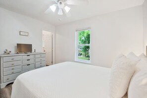 A bedroom with a bed, dresser, television, and a window with a view of greenery. - Bayou Villa w/ Dock, Kayaks & Fire Pit Fun (Pensacola)
