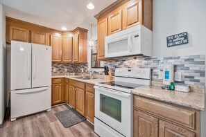 A kitchen with wooden cabinets, a white refrigerator, a microwave, an oven, and a tiled backsplash. - Bayou Villa w/ Dock, Kayaks & Fire Pit Fun (Pensacola)