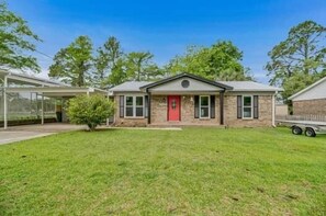 A single-story house with a red door, a covered porch, and a small front yard.