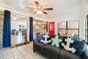A living room with a dark sofa, decorative pillows, a ceiling fan, and a brick wall.