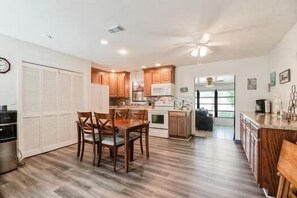 A modern kitchen with wooden cabinets, a dining area with chairs, and a visible clock on the wall.
