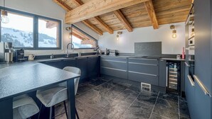 Une cuisine moderne avec un sol carrelé en pierre, des poutres en bois au plafond et une grande fenêtre donnant sur un paysage enneigé.