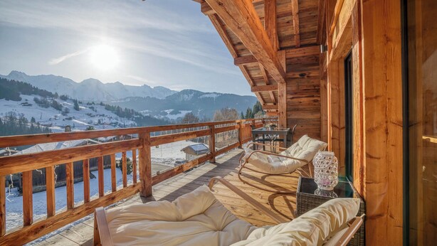 Un balcon en bois avec un canapé et une table, donnant sur un paysage montagneux enneigé.