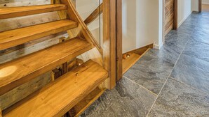 Un escalier en bois avec une rampe en verre, menant à une porte dotée d’un cadre en bois.