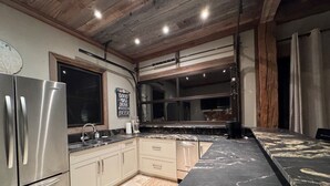 A modern kitchen with stainless steel appliances, a marble countertop, and a wooden ceiling.