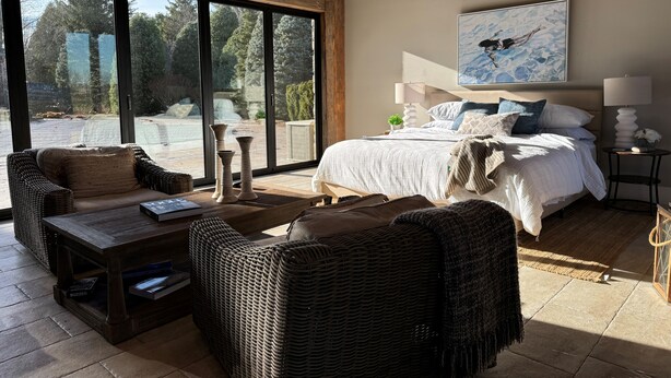 A spacious room with a large bed, a sofa, a coffee table, and a view through large windows.
