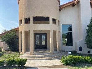 A building with a circular tower, a front door with glass panels, and a paved entrance area.