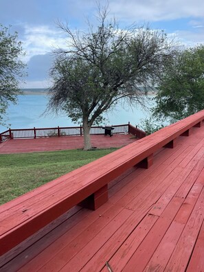 A red wooden deck with benches overlooking a body of water, a tree, and a fenced area.