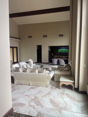 A spacious living room with a large TV, comfortable seating, and a tiled floor.