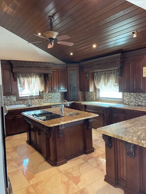 A spacious kitchen with dark wood cabinets, a central island with a sink, and a ceiling fan.
