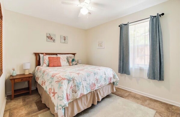 A bedroom with a bed, a nightstand, a ceiling fan, and a window with curtains. - 3 bedroom house in Oak Island, NC. Close to Beach, Family Friendly & Firepit (Oak Island)