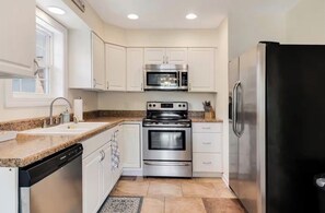A compact kitchen with white cabinets, a stainless steel refrigerator, a microwave, an oven, and a dishwasher.