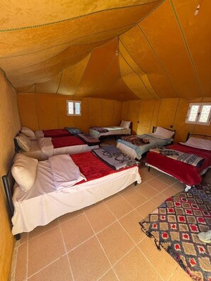 A tent with four beds, each with a pillow and blanket, and a patterned rug on the floor. - Typical Merzouga Camp (Merzouga)