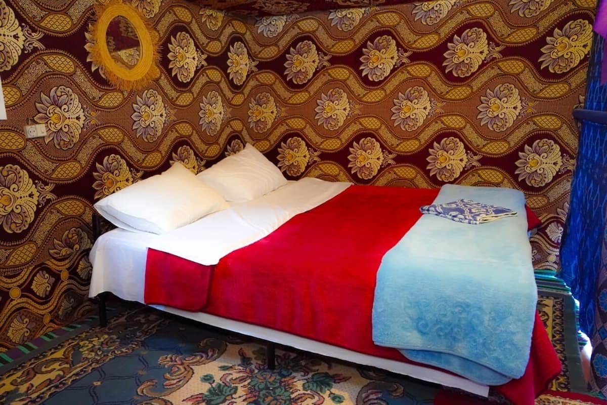 Uma cama com um cobreleito vermelho e branco, uma toalha azul e um papel de parede estampado.