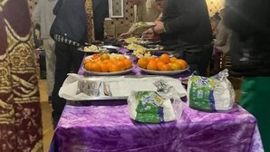 Una habitación con elaborados diseños en el techo, una mesa con comida y gente reunida alrededor.