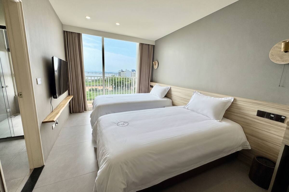 Habitación de hotel con dos camas, televisión, balcón con vistas y un diseño moderno.