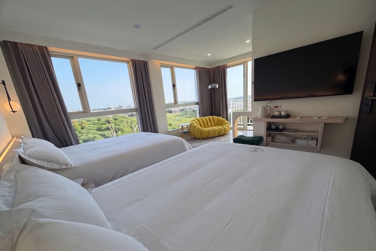 Habitación de hotel con dos camas, un televisor de pantalla plana, un escritorio con hervidor y una silla.
