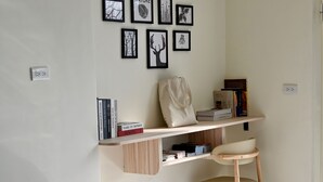 A room with a round, plush seating area, a wooden chair, a shelf with books and a handbag, and framed pictures on the wall. - CP Tide whisper (Jinning)