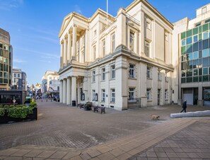 Ein historisches Gebäude mit klassischer Architektur, ein gepflasterter Platz und Bänke.