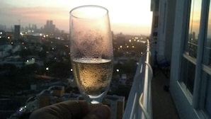 A hand holding a glass of champagne with a cityscape view in the background. - Cozy Apartment Near the Beach, Pool Access, Hot Water (Cartagena)