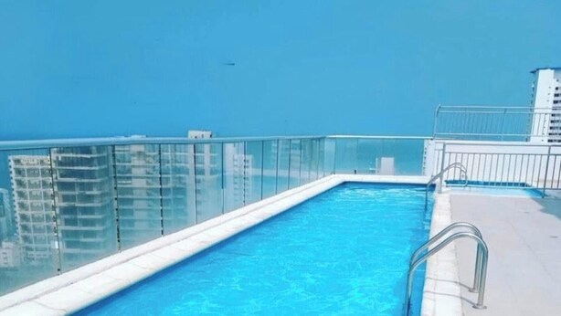 A rooftop pool with clear blue water, a glass railing, and a view of the city skyline. - Cozy Apartment Near the Beach, Pool Access, Hot Water (Cartagena)