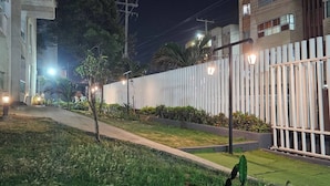 A nighttime view of a residential area with a well-lit pathway, a gated fence, and greenery. - Cozy Apartment Near the Beach, Pool Access, Hot Water (Cartagena)