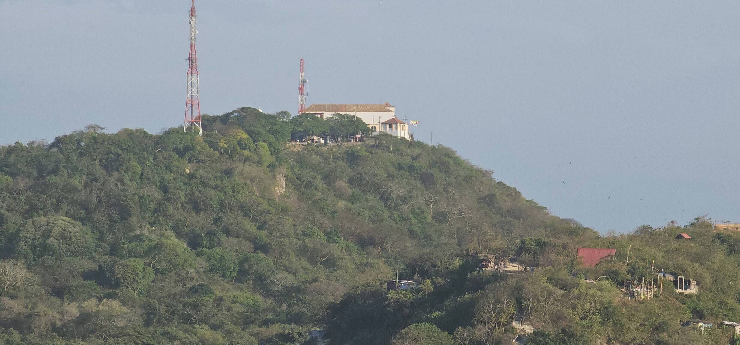 Un edifici damunt d'un turó amb teulada vermella, envoltat de vegetació espessa.