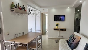 A modern living room with a dining area, a TV mounted on the wall, and a sofa with a cushion. - Apartment With Great View Near Beach & Walled City (Cartagena)
