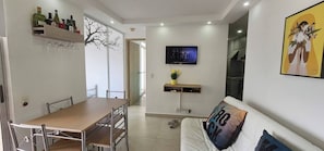 Ein modernes Wohnzimmer mit Essbereich, einem an der Wand montierten Fernseher und einer Couch mit Kissen.