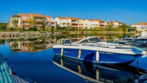 A marina with a boat docked, buildings in the background, and calm water reflecting the scene. - Mediterranean Escape in Le Barcares (Le Barcares)