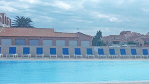 A swimming pool with lounge chairs, a tiled roof building, and other residential buildings in the background. - Mediterranean Escape in Le Barcares (Le Barcares)
