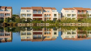 A row of multi-story buildings with balconies, a calm body of water in the foreground, and a clear blue sky. - Mediterranean Escape in Le Barcares (Le Barcares)