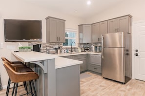 A modern kitchen with grey cabinets, a stainless steel refrigerator, a flat-screen TV, and a bar stool. - Relax w/Panoramic Views | Hot Tub & Dog friendly (Templeton)