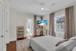 Ein Schlafzimmer mit Bett, Fernseher, Deckenventilator und einem Fenster mit Vorhängen.