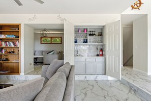 Una sala de estar con sofá, estantería y una zona de cocina con armarios y encimera.