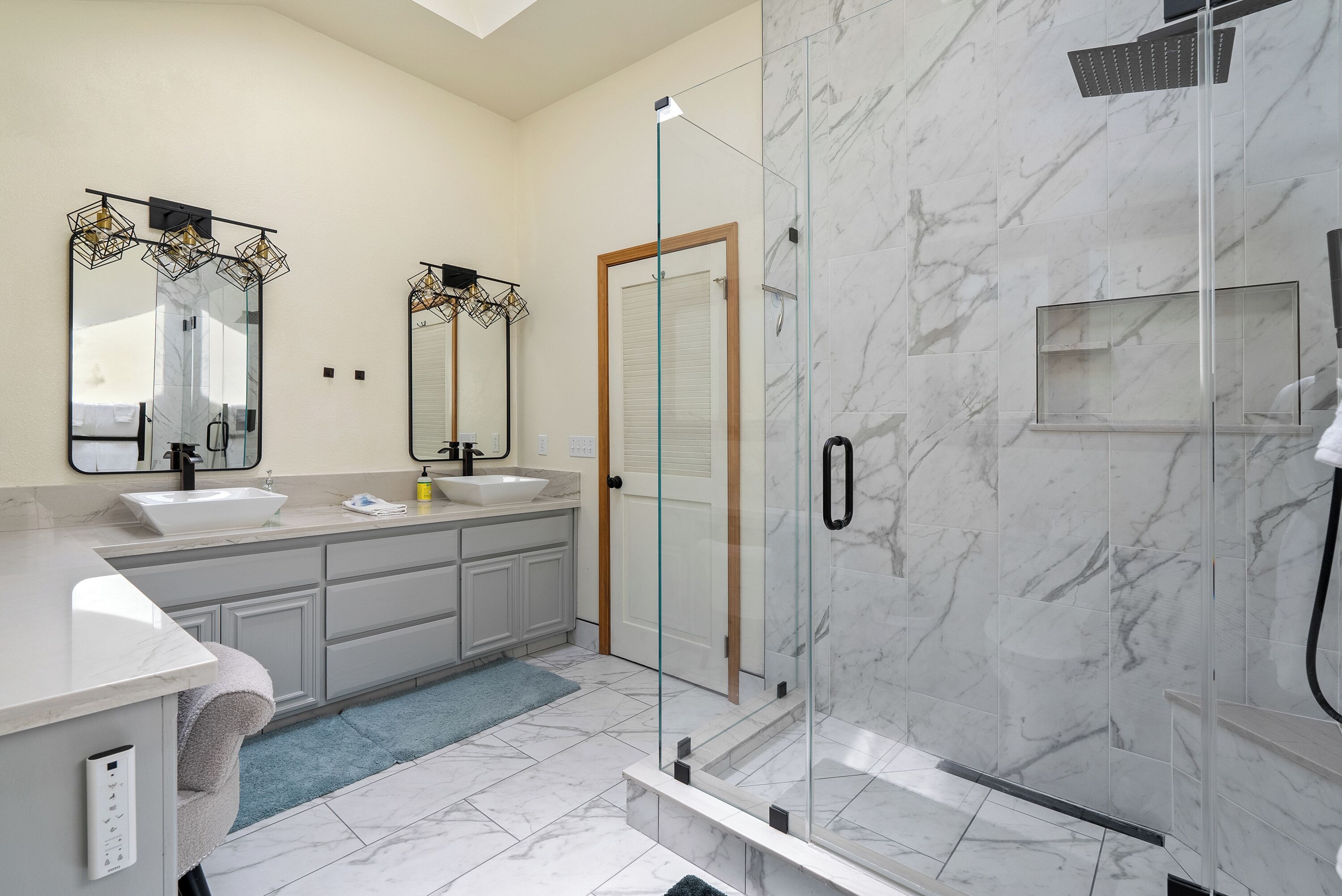 Un baño moderno con ducha de vidrio, un espejo grande y piso de mármol.