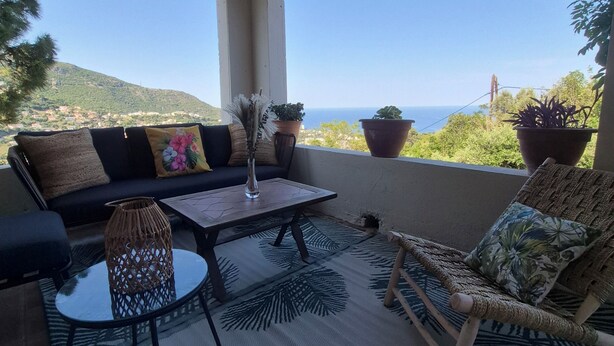 A covered outdoor seating area with a sofa, chairs, a coffee table, and potted plants.