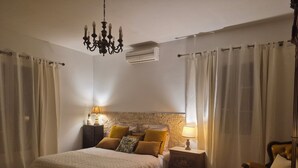 A bedroom with a bed, nightstands, a chair, a chandelier, and curtains.
