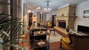 A living room with a fireplace, a sofa, a yellow armchair, a TV, and a chandelier.