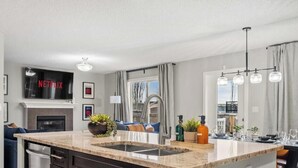 Une cuisine moderne dotée d’un four encastré, d’un grand îlot central avec un évier et d’un téléviseur à écran plat fixé au-dessus du four.
