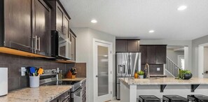 A modern kitchen with dark cabinetry, stainless steel appliances, and a granite countertop. - Game Night Getaway - HotTub - AC - BBQ - Firetable - KingBed (Edmonton)