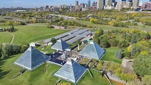 Un vaste complexe immobilier composé de plusieurs structures en forme de pyramide, entouré d’espaces verts et avec une vue sur les gratte-ciel de la ville en arrière-plan.