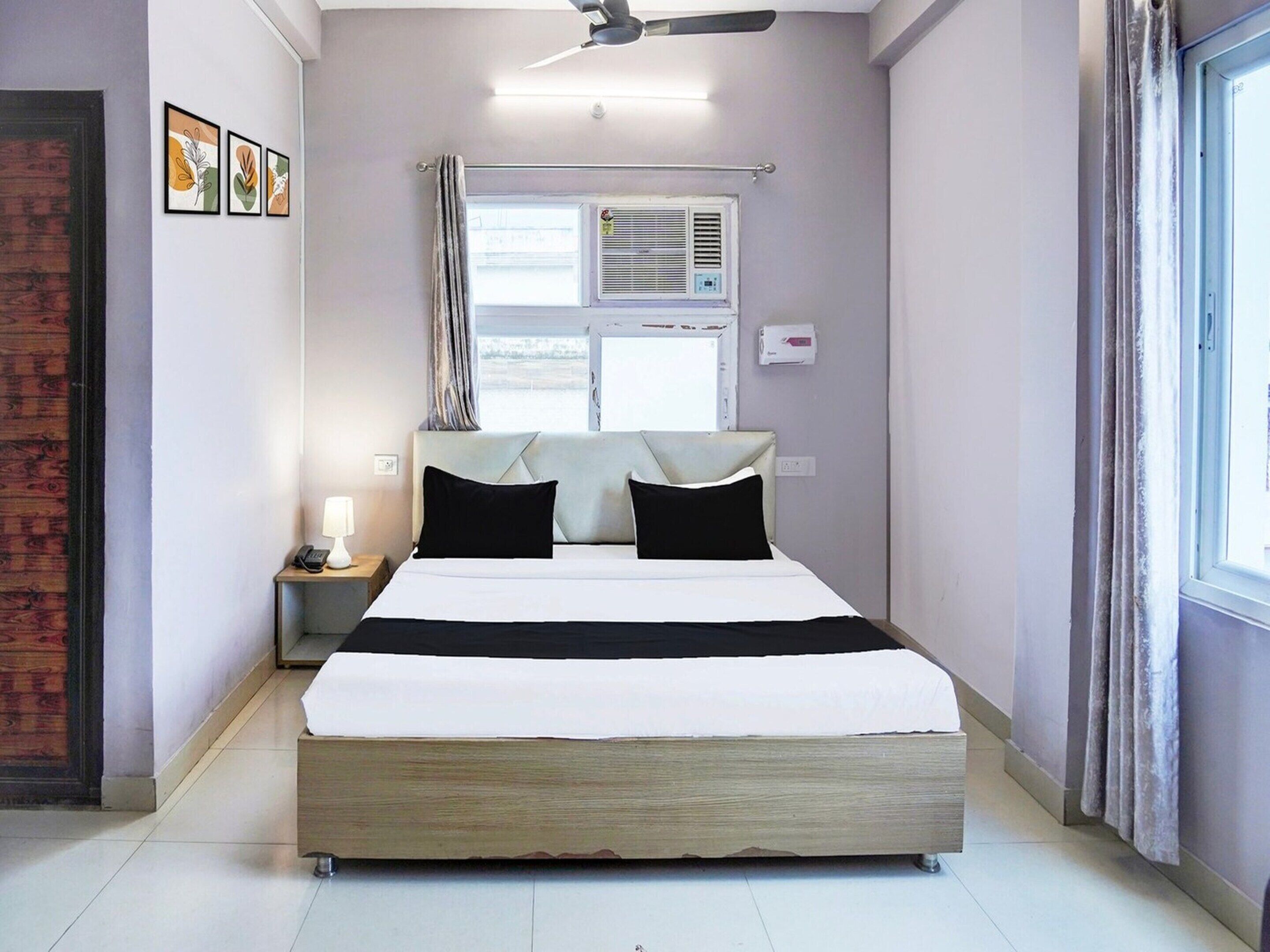 Une chambre à coucher comprenant un lit, une table de chevet, une lampe, un climatiseur et un ventilateur de plafond.