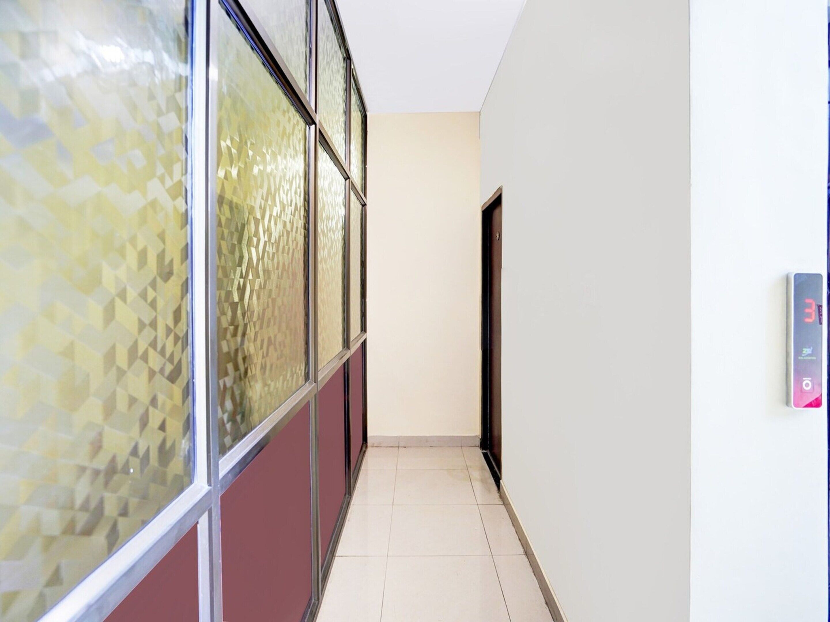 A hallway with patterned glass windows, a tiled floor, and a wall-mounted elevator control panel.