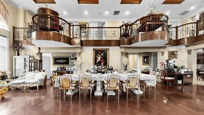 A spacious dining area with a high ceiling, ornate railings, and a chandelier.