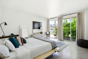 A modern bedroom with a bed, bedside tables, a lamp, a mirror, and a view of the outdoors. - Mid-Century Retreat Near El Paseo (Palm Desert)
