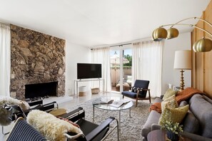 A modern living room with a stone wall, a flat-screen TV, a sofa, a coffee table, and a fireplace. - Mid-Century Retreat Near El Paseo (Palm Desert)