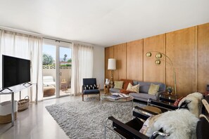 A modern living room with a flat-screen TV, a sofa, a coffee table, and a lamp. - Mid-Century Retreat Near El Paseo (Palm Desert)