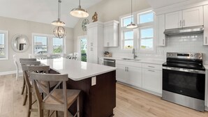 A modern kitchen with white cabinets, a large island, stainless steel appliances, and pendant lighting. - Saltwater Pool | Hot Tub | Rec Room | Dogs OK (Corolla)