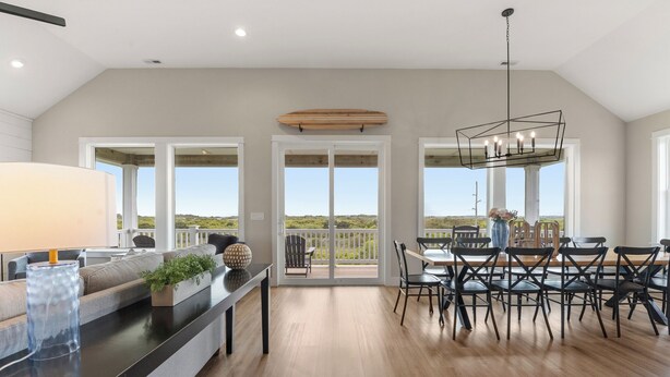 A spacious room with a dining area, a sofa, a coffee table, and a view through large glass doors. - Sunset State of Mind: Private Pool | Hot Tub | Elevator (Nags Head)
